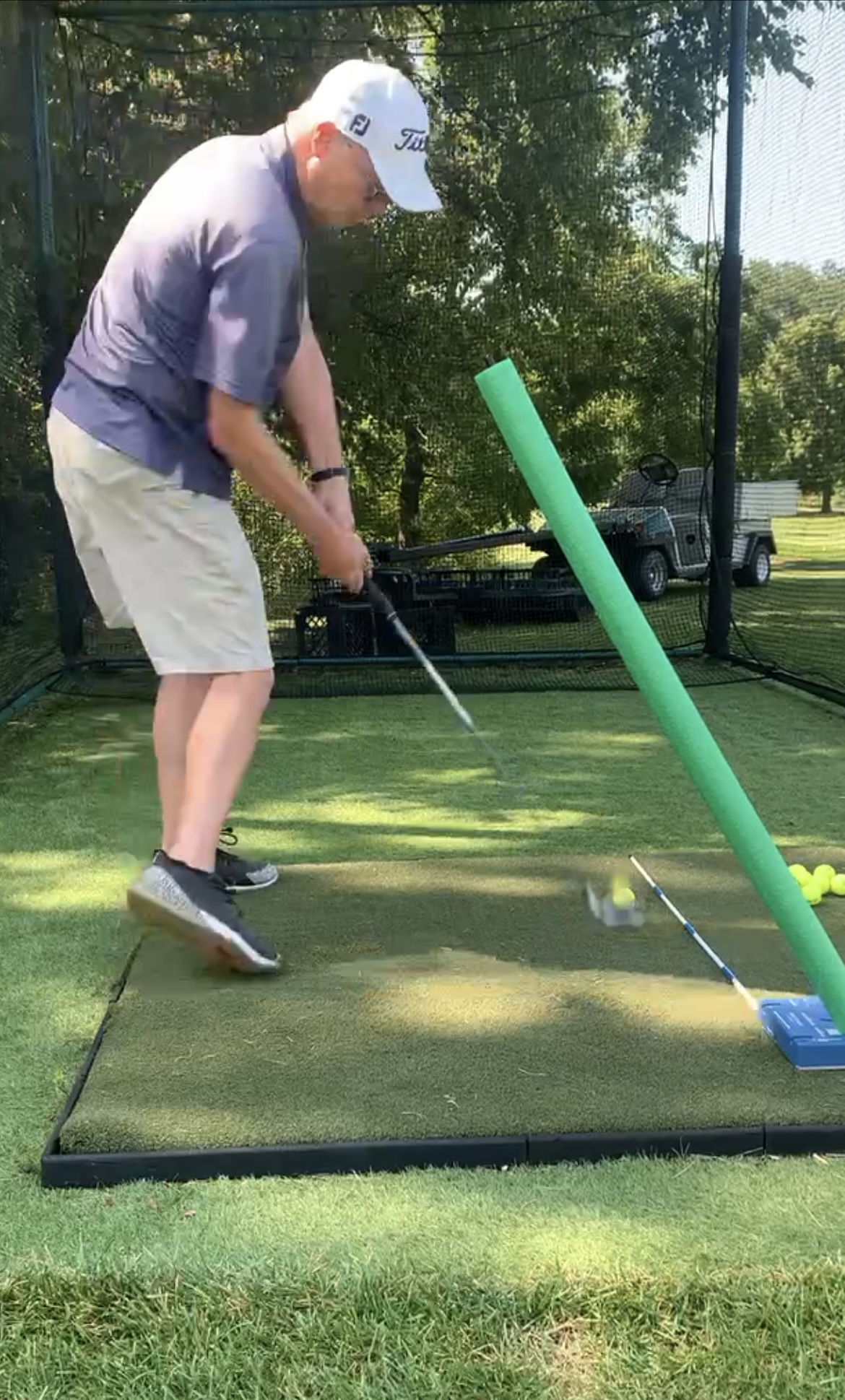 Golfer hitting a shot with a foam noodle and alignment stick as swing constraints
